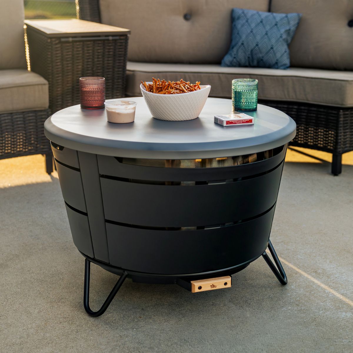 TIKI Brand Reunion Tabletop Cover Gray on fire pit, used as table with snacks and drinks outdoors