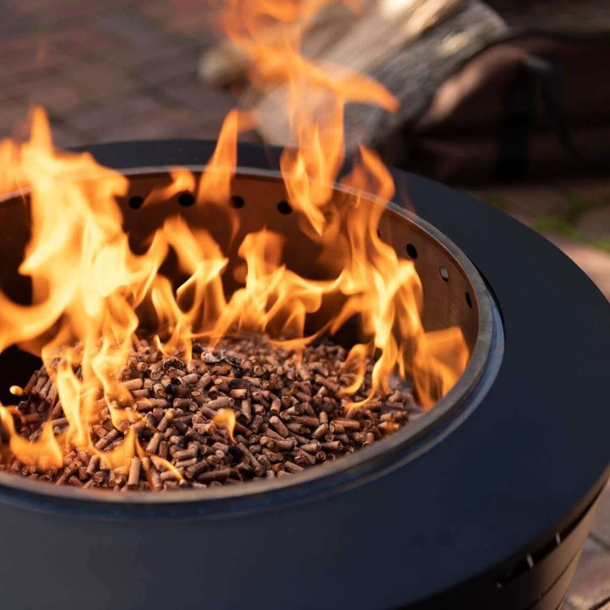 Close-up of a TIKI fire pit burning wood pellets, with bright flames and a sleek black metal rim.
