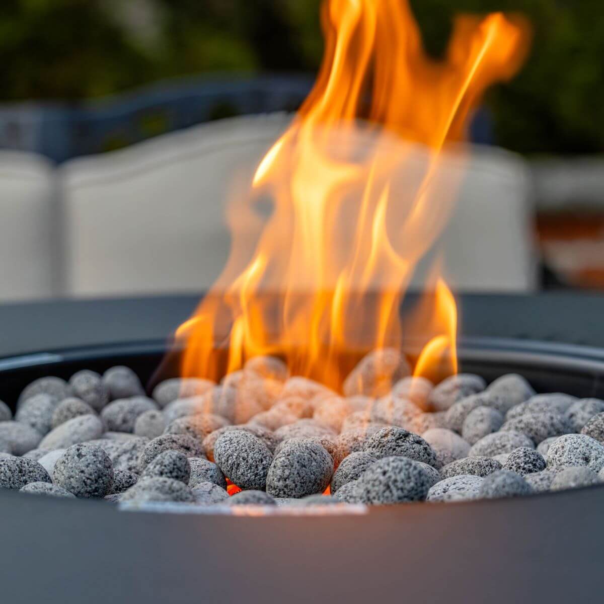 Outdoor fire pit with glowing orange flames and gray lava rocks.