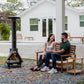 Couple relaxes on outdoor bench near a TIKI Brand smokeless fire pit, enjoying a cozy backyard setting.