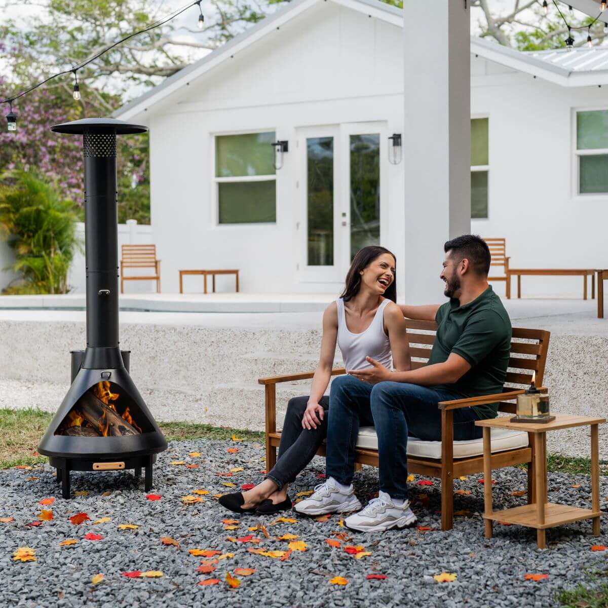 Couple relaxes on outdoor bench near a TIKI Brand smokeless fire pit, enjoying a cozy backyard setting.
