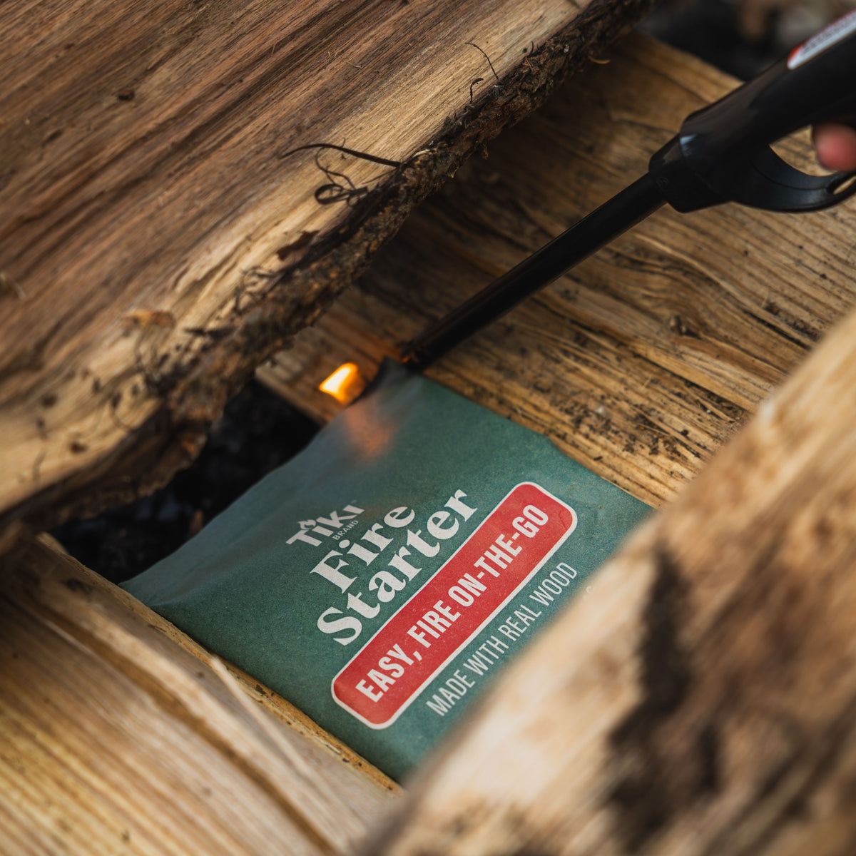 Green Tiki Fire Starter packet with "EASY FIRE ON-THE-GO" text, surrounded by wood.