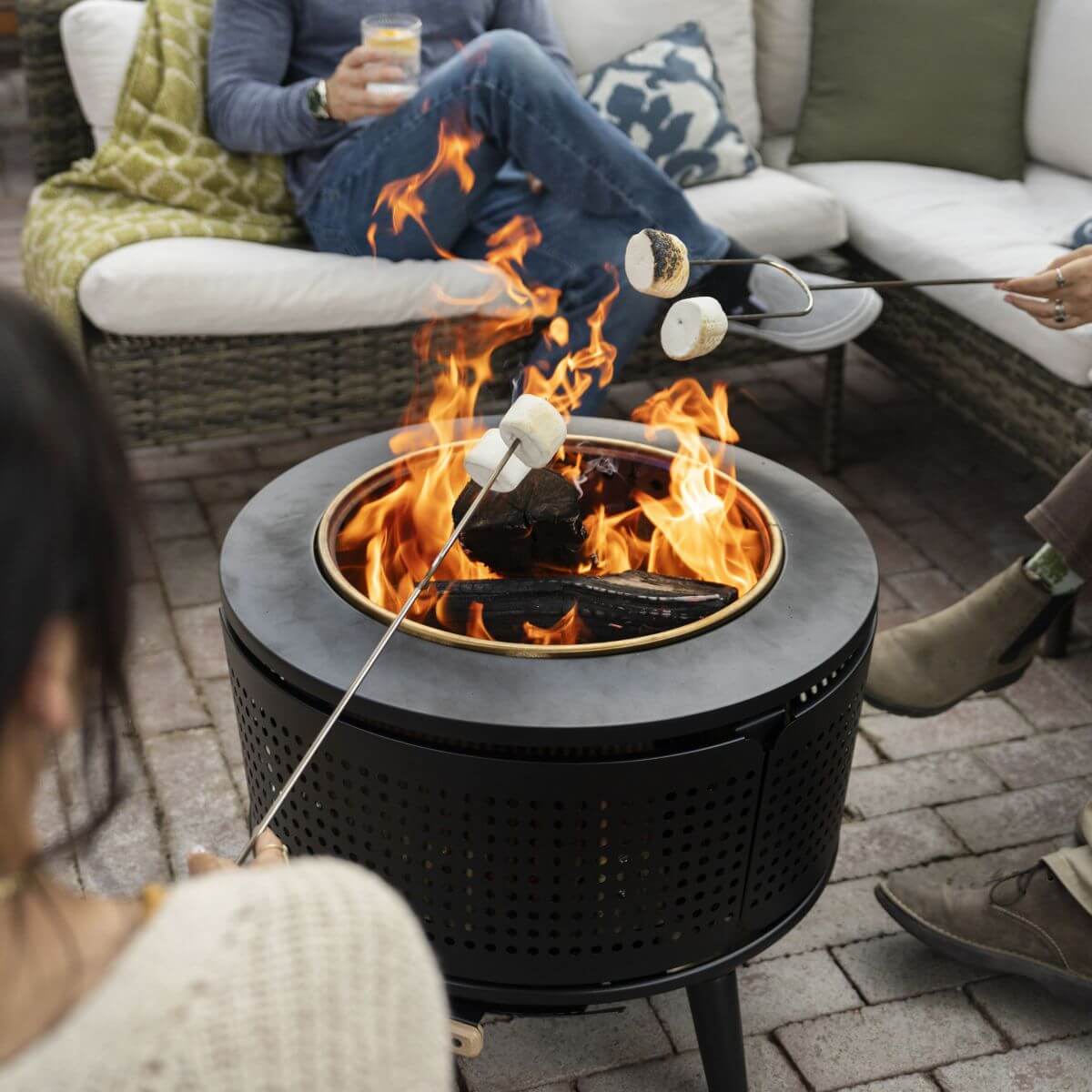 People roasting marshmallows over a TIKI® fire pit on a patio, with outdoor seating in the background.